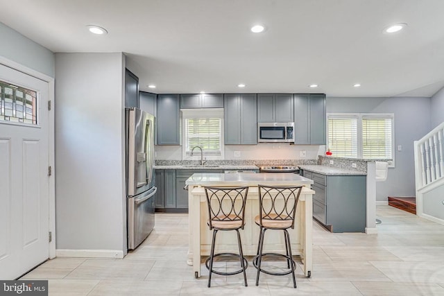  - kitchen featuring stainless steel appliances, a breakfast bar area, gray cabinetry, a kitchen island, and recessed lighting
