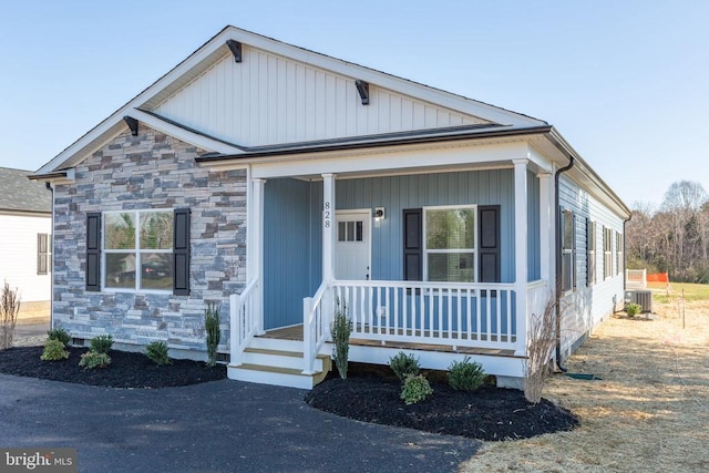 view of front facade featuring central air condition unit, covered porch, and stone siding