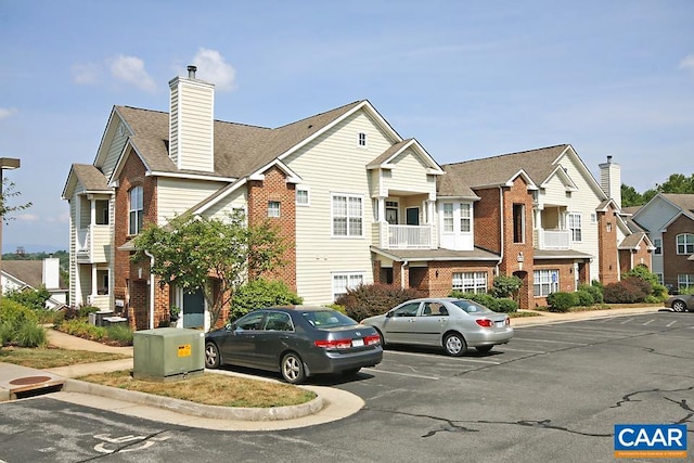 view of front of property featuring uncovered parking, a chimney, brick siding, and a residential view