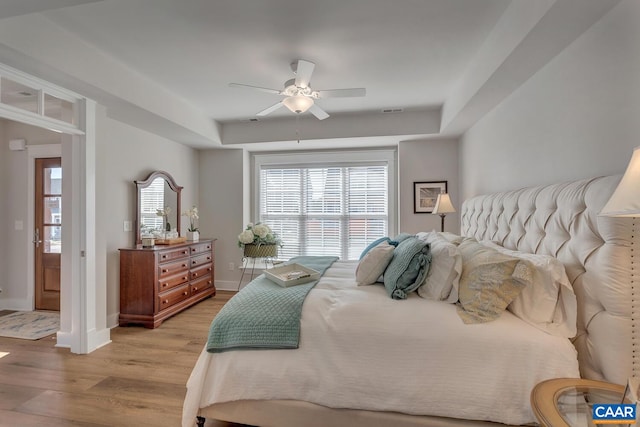 bedroom featuring a tray ceiling, baseboards, light wood-style flooring, and visible vents