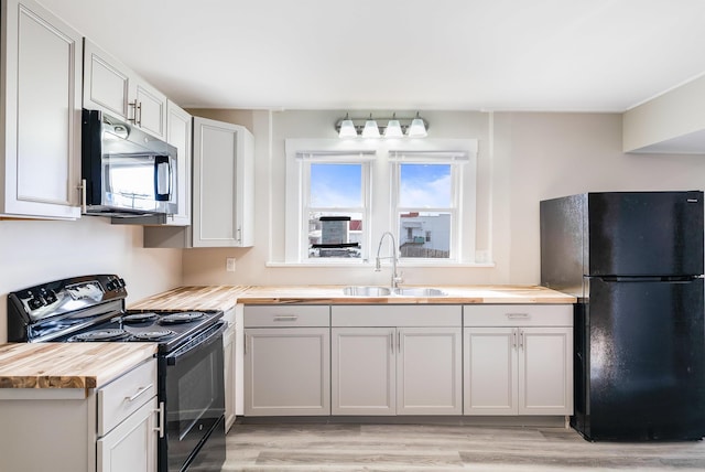 kitchen with butcher block countertops, light wood finished floors, a sink, and black appliances