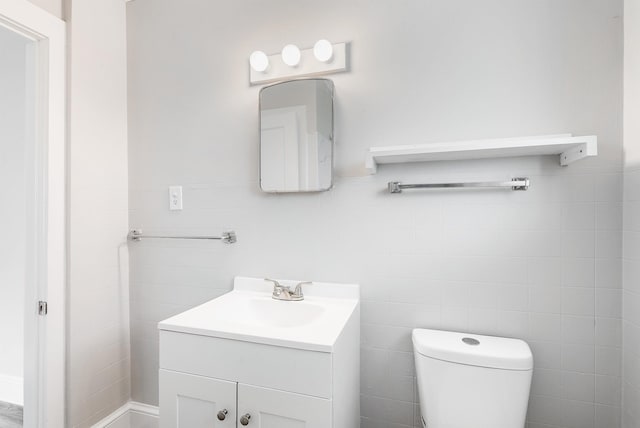 half bath featuring vanity, toilet, and tile walls
