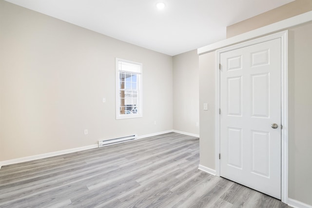 unfurnished bedroom with a baseboard heating unit, light wood-style floors, and baseboards