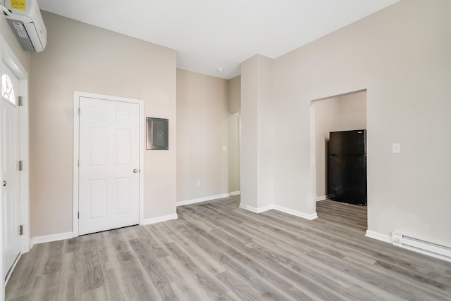 unfurnished living room featuring electric panel, a baseboard radiator, light wood-style flooring, a wall mounted AC, and baseboards