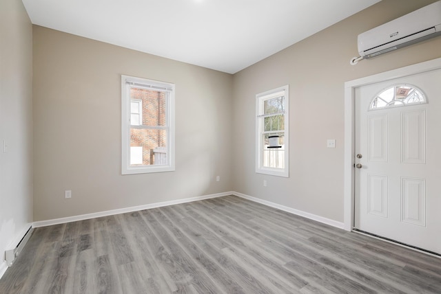 foyer with a baseboard heating unit, baseboards, wood finished floors, and an AC wall unit