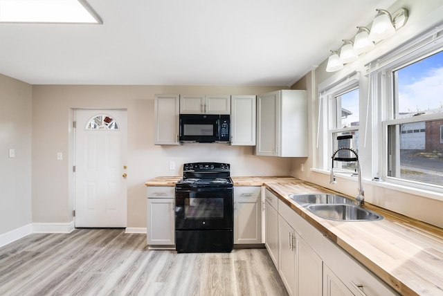 kitchen with a sink, light wood finished floors, wooden counters, and black appliances