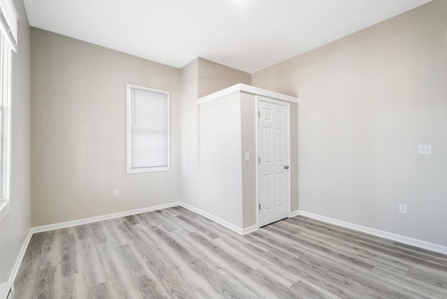 unfurnished room with baseboards, a baseboard radiator, and light wood-type flooring