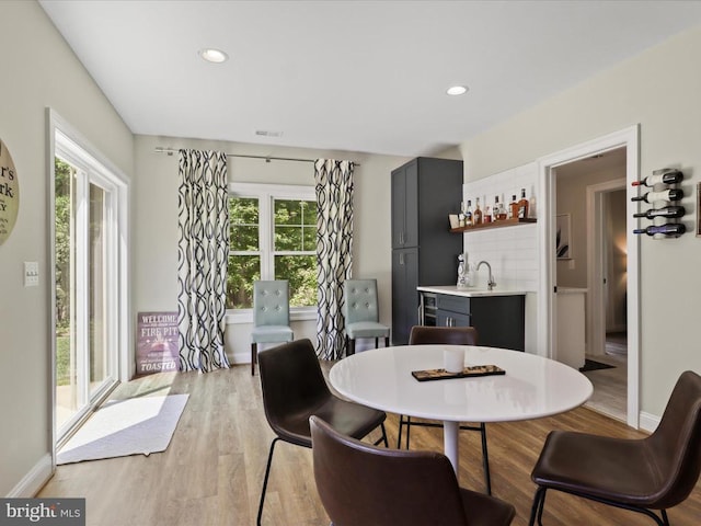 dining room featuring bar with sink, light wood-type flooring, recessed lighting, and baseboards