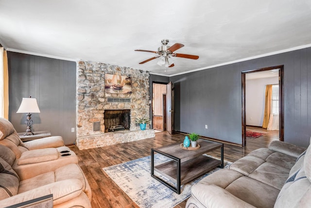 living room with crown molding, a stone fireplace, wood-type flooring, and ceiling fan