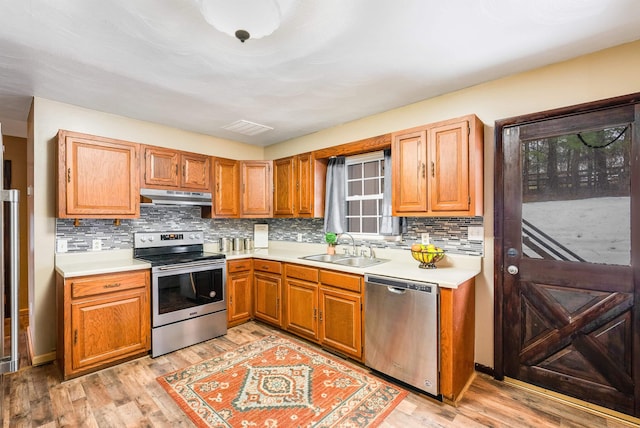 kitchen with backsplash, stainless steel appliances, sink, and light wood-type flooring