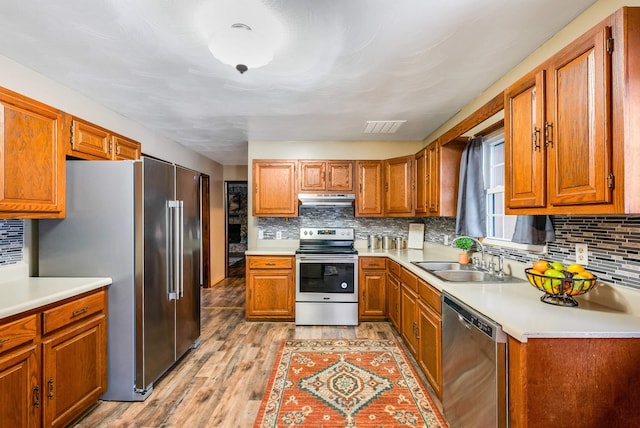 kitchen with tasteful backsplash, appliances with stainless steel finishes, sink, and light hardwood / wood-style flooring