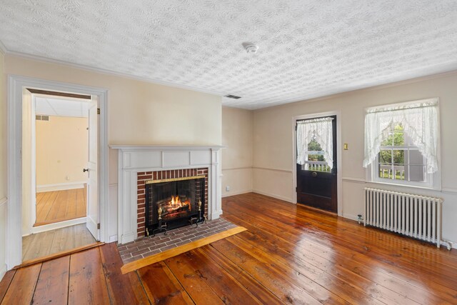 887 Natural Chimneys Rd, Mount Solon, VA 22843 - unfurnished living room featuring radiator heating unit, wood-type flooring, a textured ceiling, a brick fireplace, and ornamental molding