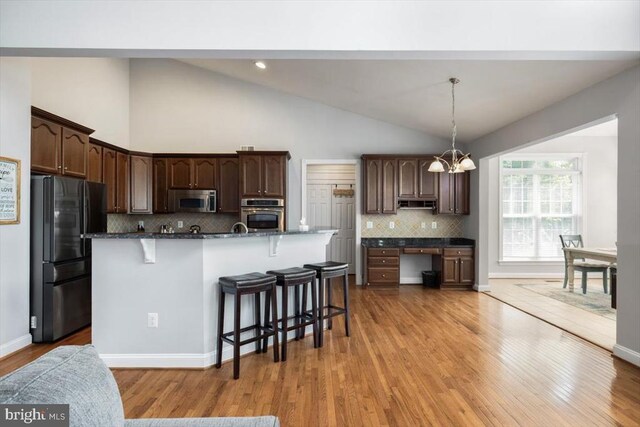  - kitchen with appliances with stainless steel finishes, a kitchen bar, light wood-style flooring, tasteful backsplash, and dark brown cabinets