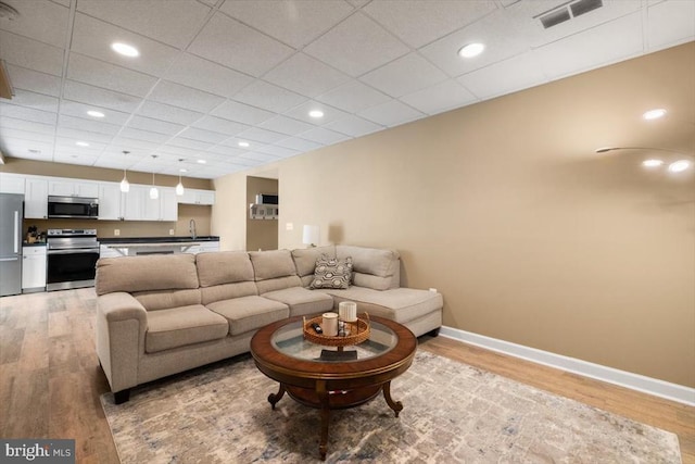  - living area with light wood-style flooring, baseboards, a drop ceiling, and recessed lighting