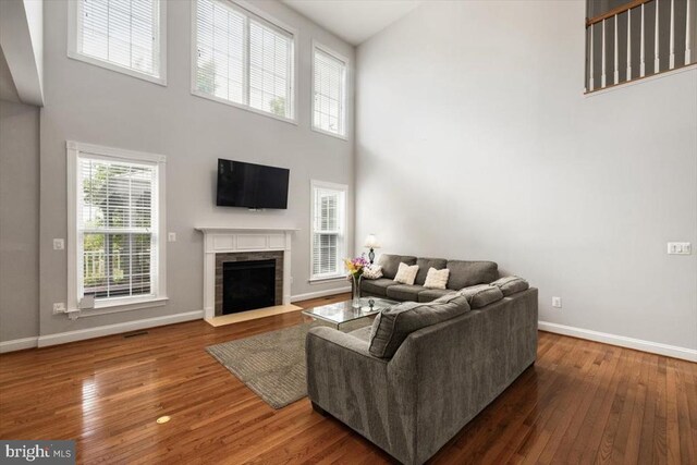  - living area featuring a high ceiling, wood-type flooring, baseboards, and a fireplace with flush hearth