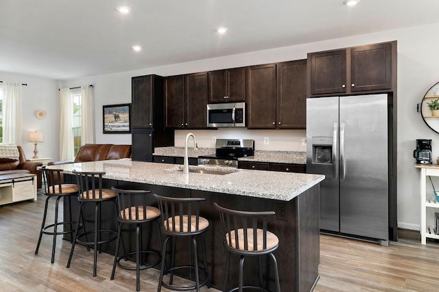 301 Willowshire Ct, Waynesboro, VA 22980 - kitchen with appliances with stainless steel finishes, light wood-style floors, dark brown cabinets, a breakfast bar area, and a kitchen island with sink