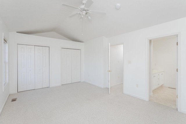 unfurnished bedroom with ensuite bathroom, two closets, lofted ceiling, ceiling fan, and light carpet