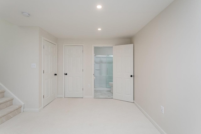 unfurnished bedroom with light colored carpet, a closet, and ensuite bathroom