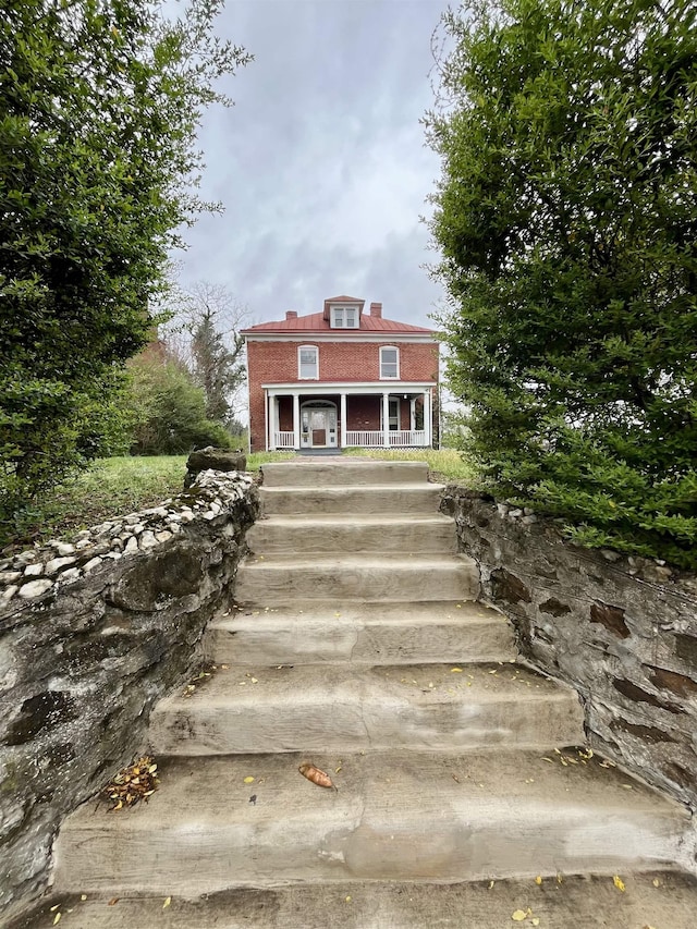 view of front of house with a porch, brick siding, and stairway