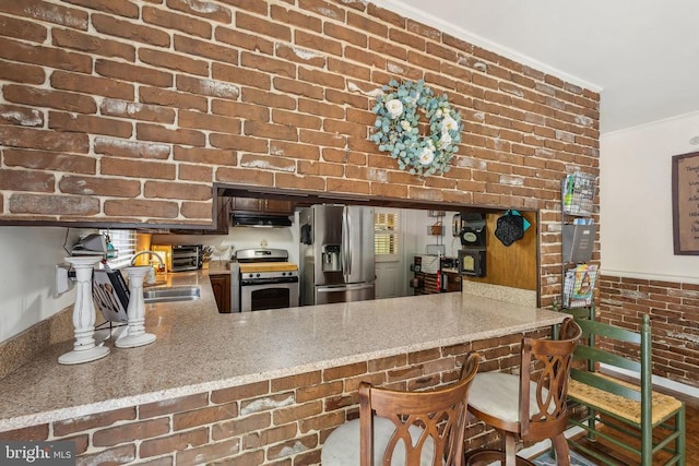 - kitchen featuring appliances with stainless steel finishes, under cabinet range hood, a peninsula, and brick wall