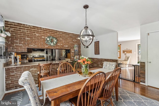  - dining space featuring brick wall, wood finished floors, and a chandelier