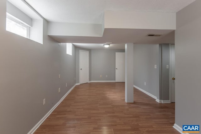 below grade area featuring wood finished floors, plenty of natural light, baseboards, and a textured ceiling