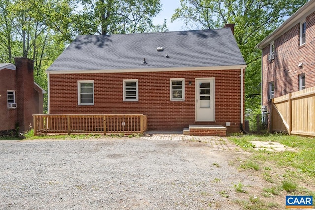 back of house with fence, a chimney, brick siding, and a shingled roof
