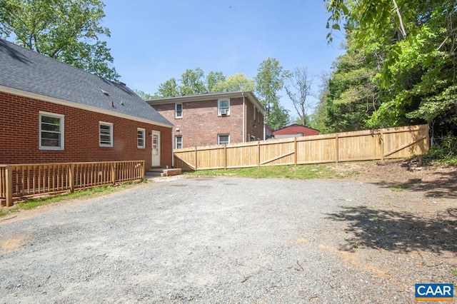 back of property featuring fence, brick siding, and roof with shingles