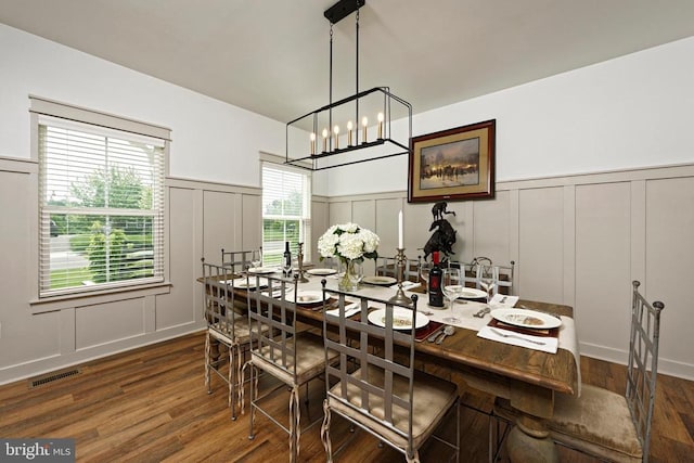  - dining area featuring a decorative wall, wainscoting, dark wood-type flooring, and a chandelier