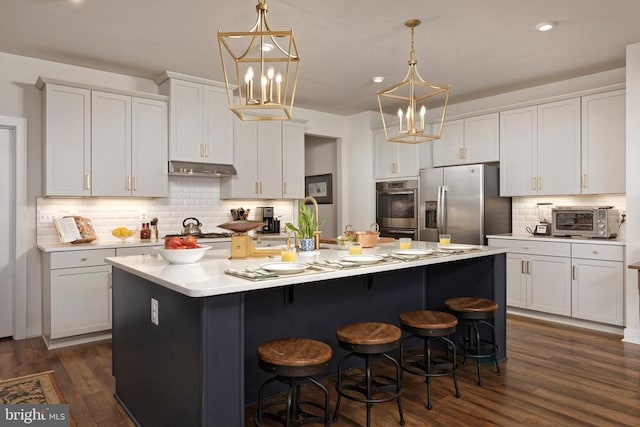  - kitchen with appliances with stainless steel finishes, backsplash, an island with sink, a breakfast bar area, and dark wood-style flooring