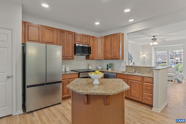 kitchen with brown cabinetry, a sink, a kitchen island, stainless steel appliances, and tasteful backsplash