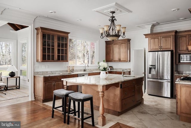 - kitchen featuring appliances with stainless steel finishes, a kitchen bar, a center island with sink, glass insert cabinets, and light stone counters