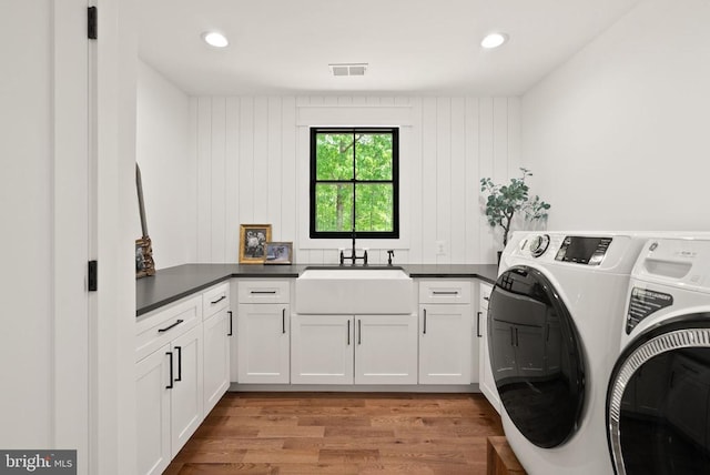  - washroom featuring a sink, cabinet space, wood finished floors, visible vents, and washer and dryer