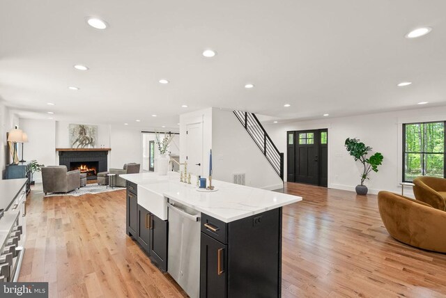  - kitchen featuring dark cabinets, light wood-style flooring, a brick fireplace, open floor plan, and stainless steel dishwasher