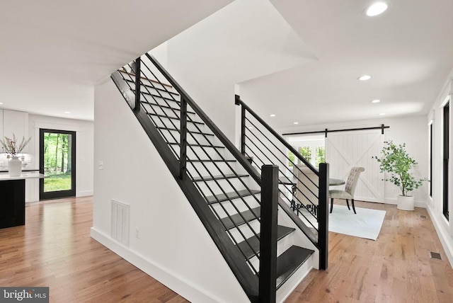  - staircase featuring wood finished floors, a barn door, visible vents, recessed lighting, and baseboards