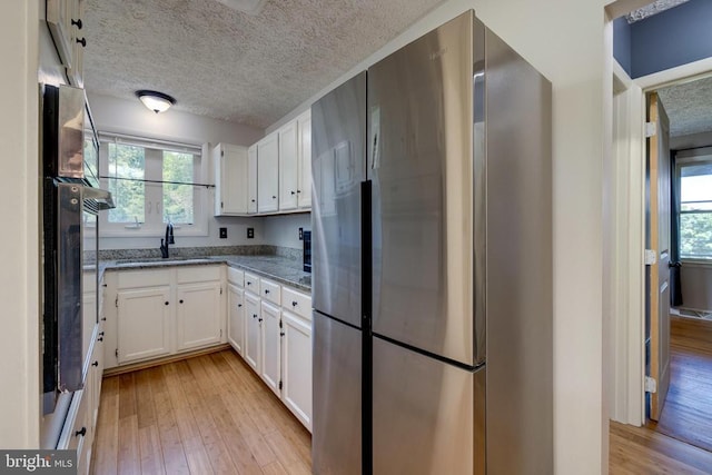 kitchen with freestanding refrigerator, a sink, plenty of natural light, white cabinets, and a textured ceiling