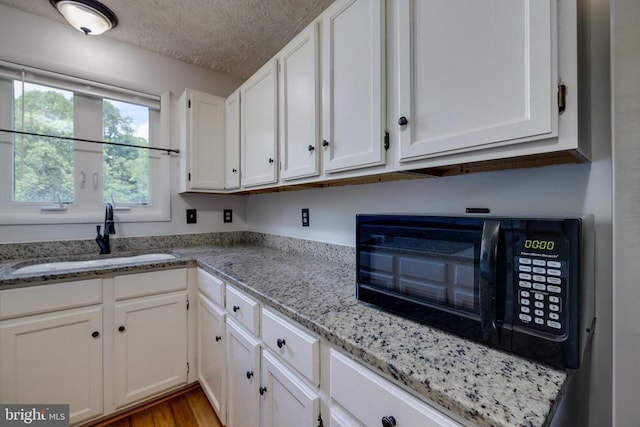 kitchen featuring a sink, white cabinetry, a textured ceiling, black microwave, and light stone countertops