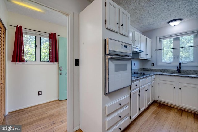kitchen with white oven, white cabinets, light wood-style floors, under cabinet range hood, and a sink