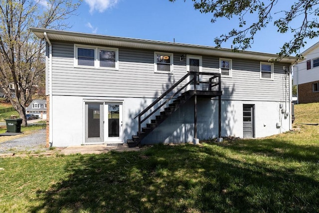 rear view of house with a lawn, stairs, and stucco siding