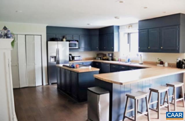 kitchen featuring a peninsula, stainless steel appliances, a kitchen breakfast bar, light countertops, and dark wood-style floors