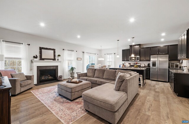 living area featuring light wood-style flooring, plenty of natural light, recessed lighting, and a fireplace with flush hearth