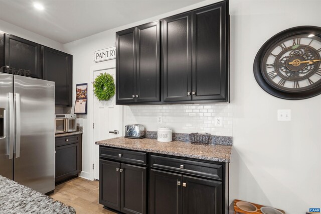 kitchen with stainless steel fridge with ice dispenser, dark cabinetry, backsplash, and light wood finished floors