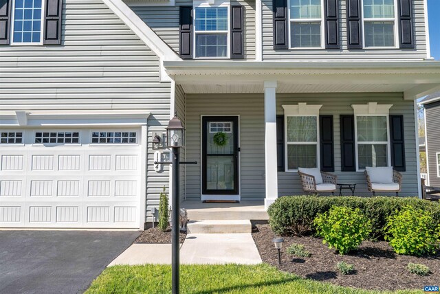 doorway to property featuring an attached garage, a porch, and driveway