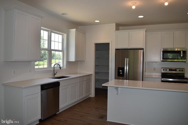 kitchen featuring stainless steel appliances, a sink, white cabinetry, dark wood-type flooring, and light countertops