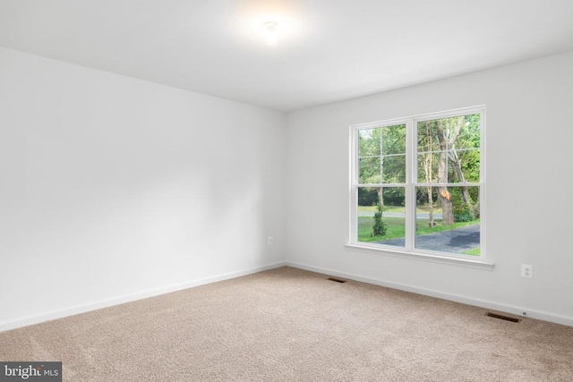 spare room with carpet floors, visible vents, and baseboards