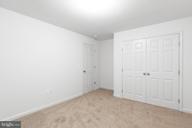 unfurnished bedroom featuring light carpet, a closet, and baseboards