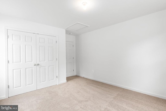 unfurnished bedroom with light carpet, attic access, baseboards, and a closet