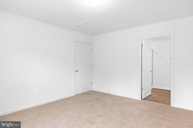 spare room with baseboards, attic access, and light colored carpet