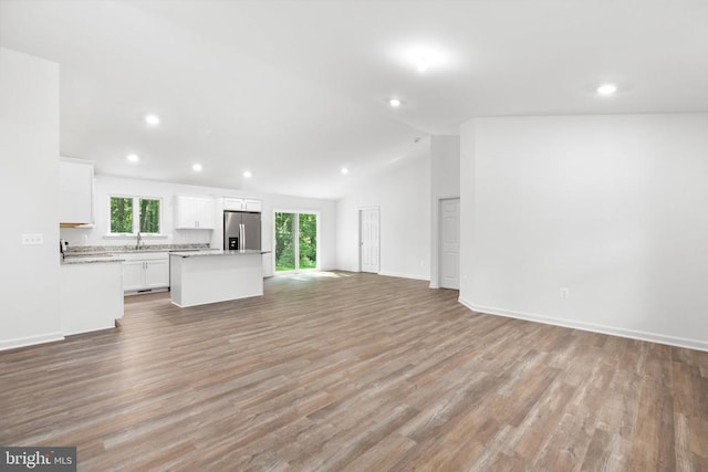 unfurnished living room featuring light wood-type flooring, vaulted ceiling, a sink, and recessed lighting