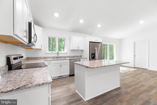 kitchen featuring a sink, a kitchen island, white cabinets, appliances with stainless steel finishes, and light stone countertops